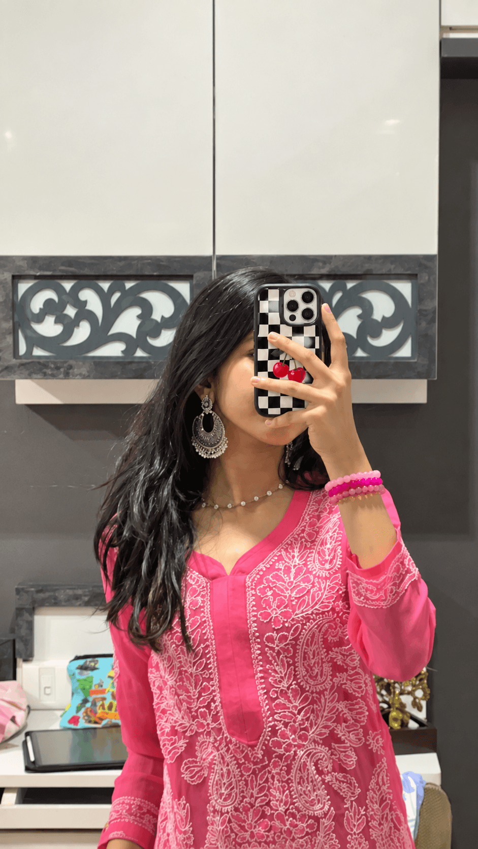 Mirror selfie featuring a black checkerboard cherry phone case with a bright pink outfit.