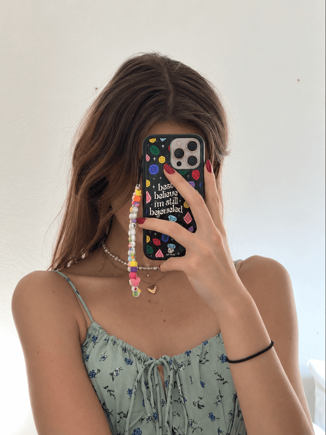 Mirror selfie featuring a black colourful jewel-inspired phone case with a pastel blue outfit.