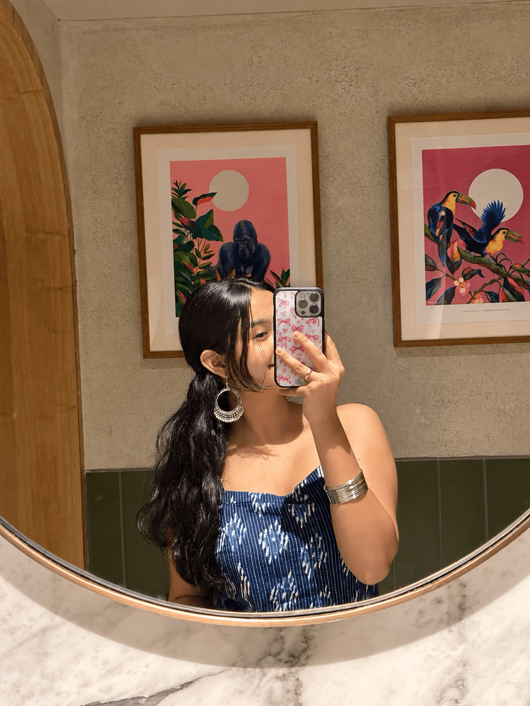 Mirror selfie featuring a pink doodle heart-inspired glass phone case with a blue patterned outfit.
